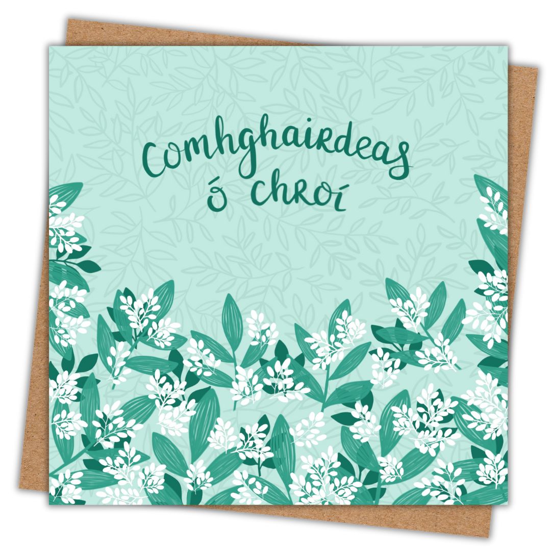 Green Irish botanical card with the words "comhgairdeas ó chroí" written in dark green hand writing. This is the Irish for Hearty Congratulations. Beneath the writing is a mixture of green and white leaves and buds. The background of the card is a light green. Behind the greeting card is a recycled Kraft brown envelope.