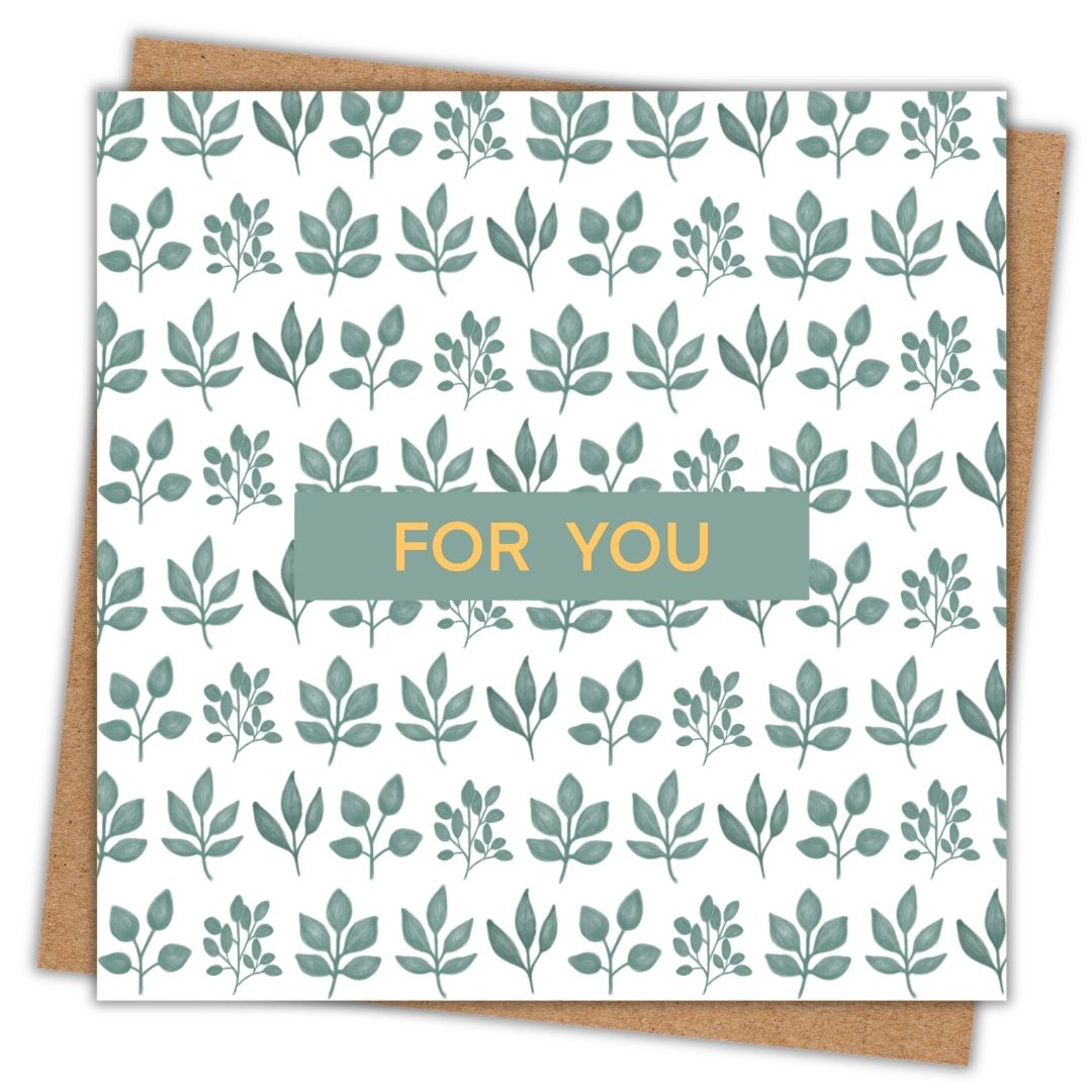 This is a patterned botanical themed greeting card for all occasions. It has the words "For You" in a simple gold font in the centre of the card on a small dark green background. Behind that, the rest of the card is a pattern on clusters of green hand drawn leaves on a white background. The card is set down on kraft brown envelope.