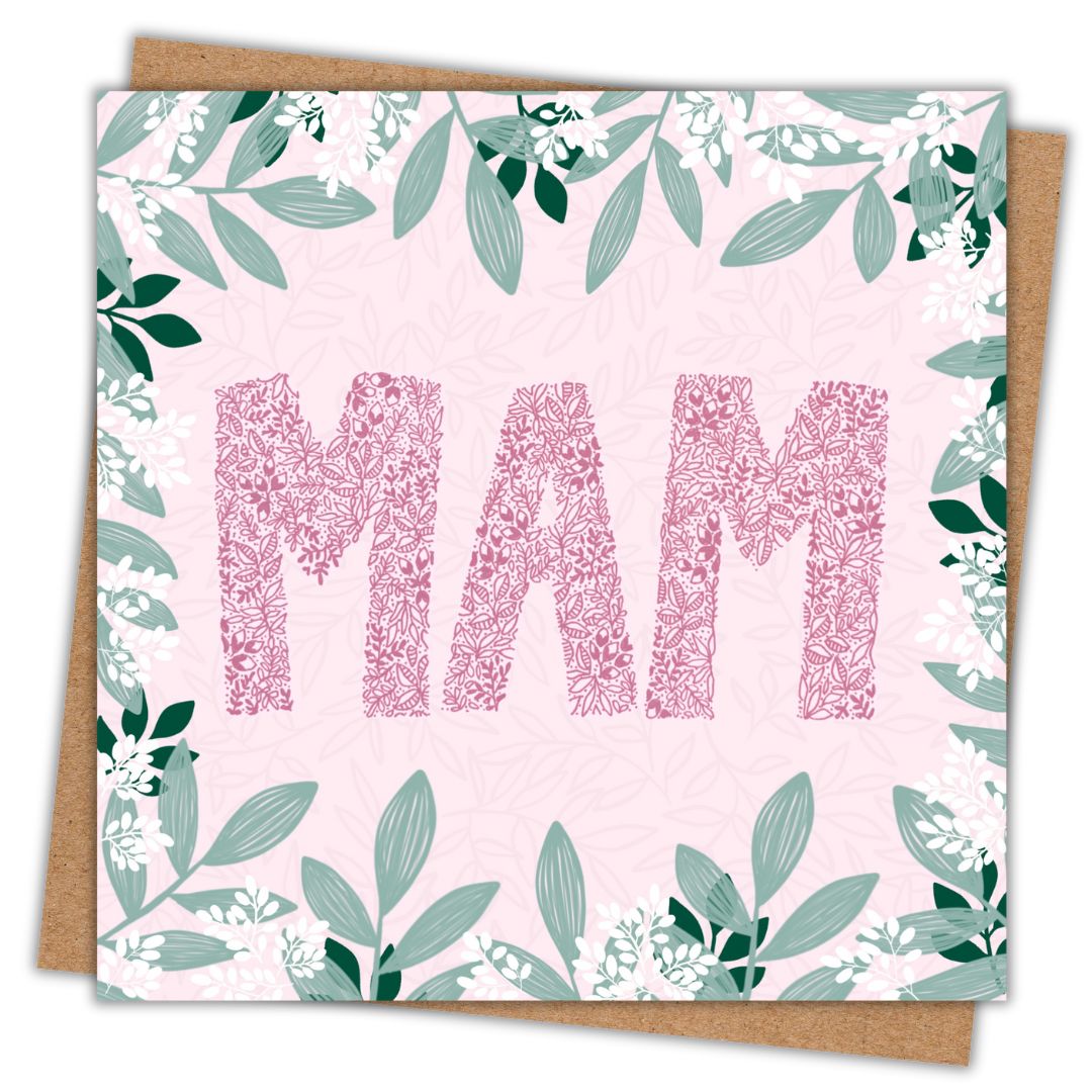 Square greeting card with the word 'MAM' in large pink floral-patterned letters on a soft pink background. The card is decorated with a border of green leaves and small white flowers. A brown kraft envelope is partially visible behind the card.