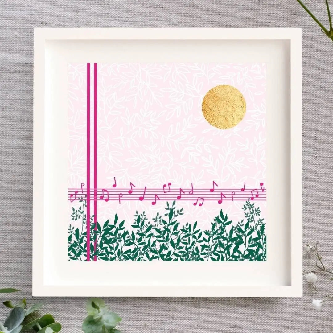 Midday Melody is a square design. The background is a soft light pink with a white leafy pattern. To the fore there are strong pink lines. Two vertical lines, and 5 horizontal lines forming a music stave with a scattering of pink notes on it. Along the bottom there are lots of green branches full of leaves. In the top right corner there is bright circle of gold leaf which has lovely texture to it. The design is framed in a white solid wood Irish made frame. It's displayed on a linen cloth.