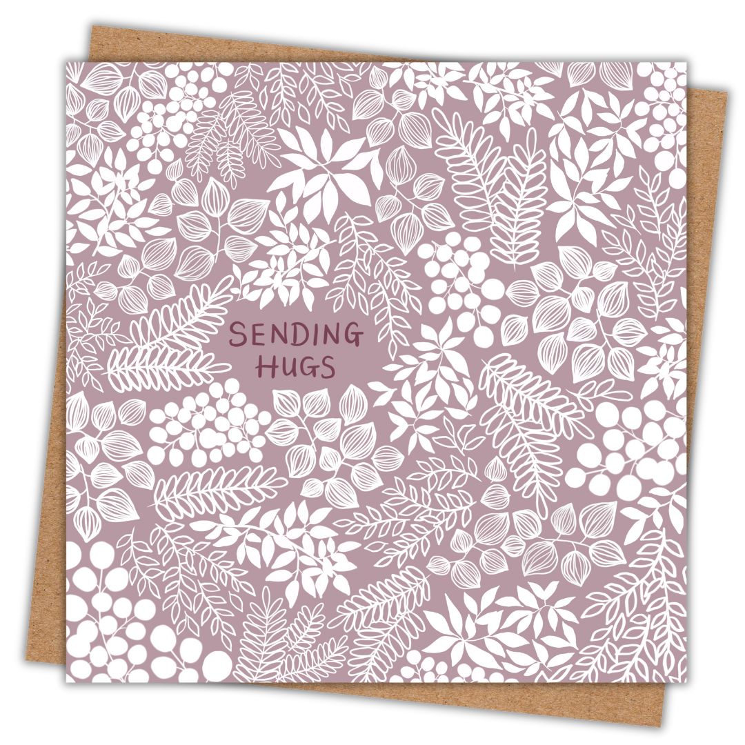 A square greeting card with a muted mauve background and intricate white floral and leafy patterns. The words 'SENDING HUGS' are centered in small, hand-written font in a deeper shade of purple-pink. The card is resting on a brown kraft envelope.