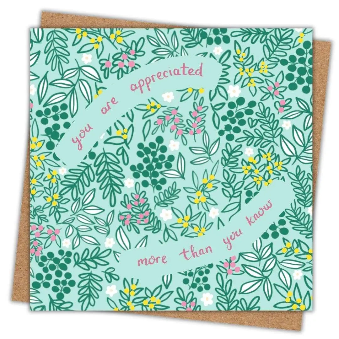 Pretty thank you card which says You Are Appreciated More Than You Know written in deep pink hand writing. The background of the card is a soft light green with dark green leaves, buds and floral details. There are scatterings of yellow and pink bud clusters as well as pretty daisy heads in between gaps in the leaves. The card is laid on a brown recycled Kraft envelope. The background is plain white.