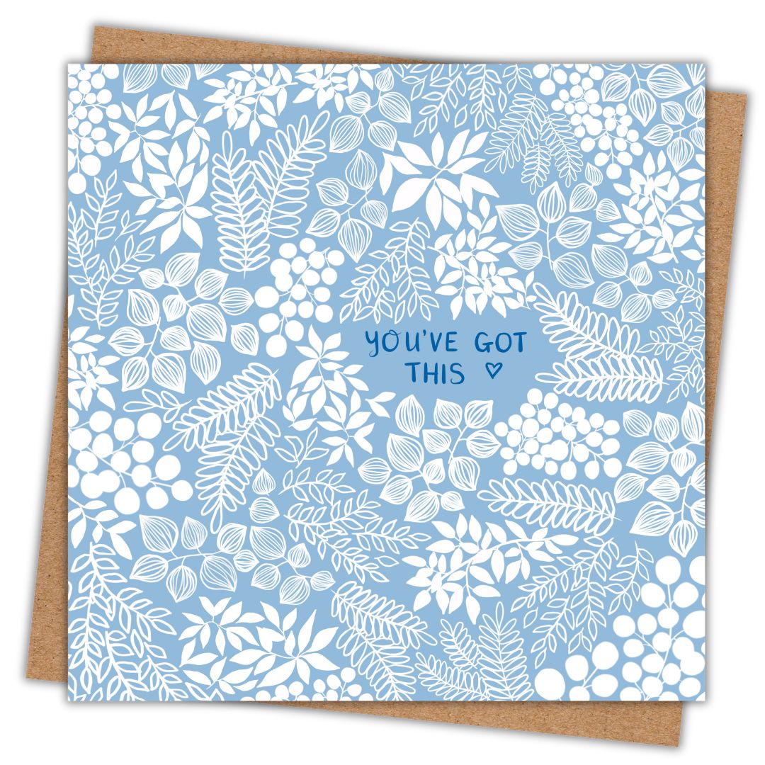A square greeting card with a soft sky blue background and intricate white floral patterns all over. The words 'You've Got this' are centered in delicate hand-writing in a true blue colour and there's a tiny love heart outline beside the words. The card is resting on a brown kraft envelope.