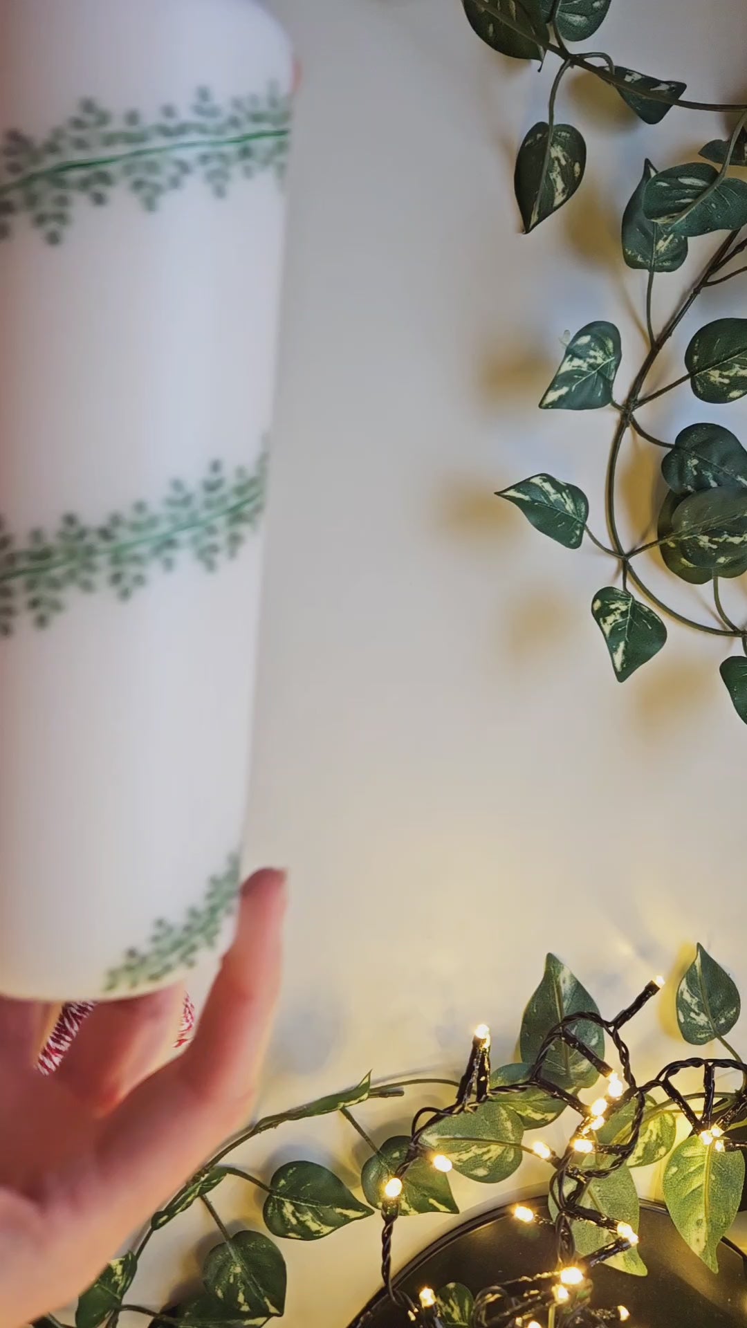Hand painted pillar candle, white, with lots of greenery in a deep green hand-painted in a garland design wrapping around the candle. The video shows a close-up of the candle design.