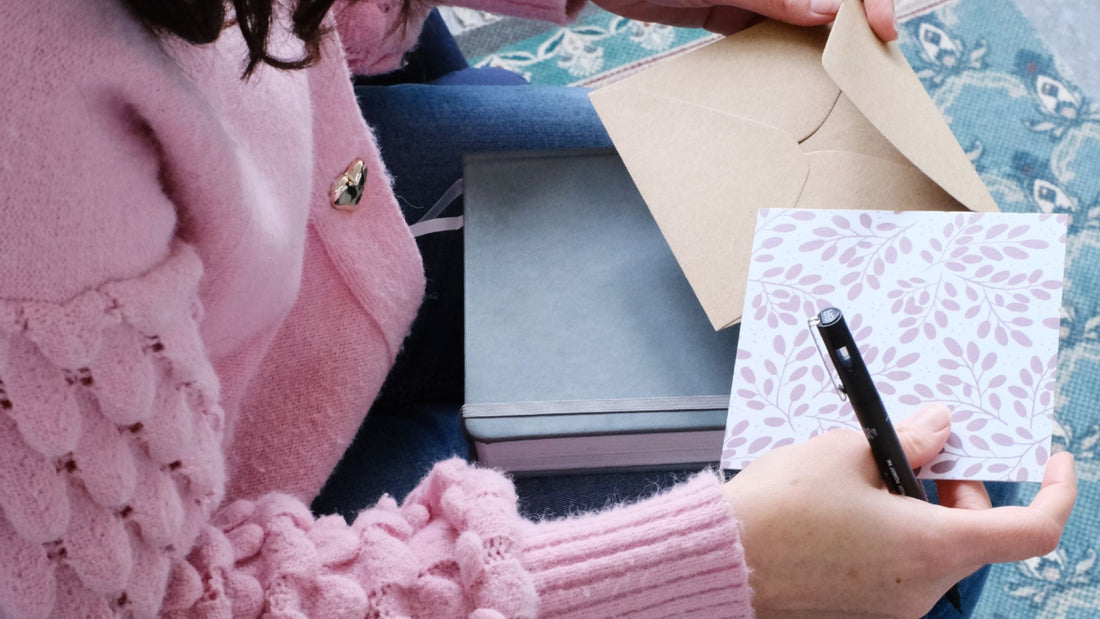 Image shows my putting a pink leafy note card into a kraft brown envelope.