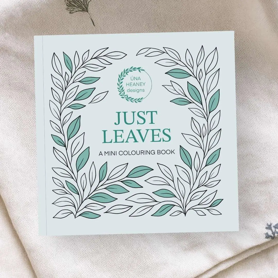 Product image of a small square colouring book. It's called Just Leaves. The cover is a light green with the title in the centre. Surrounding the title are lots of leaves, some coloured in, some not. The mini colouring book is laid on a natural cloth.