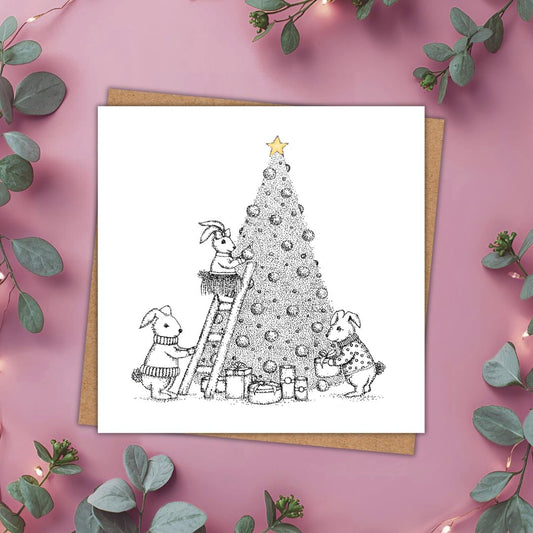 A cute little Christmas card in black and white of 3 rabbits decorating a Christmas tree. The only touch of colour is on a gold star at the top of the tree.