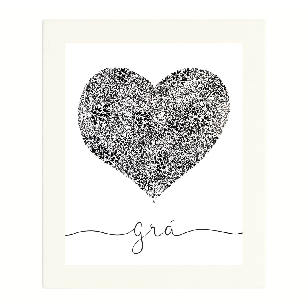 Irish language artwork in a white mount. The black and white pen illustration is in the shape of a love heart. The heart is packed full of small intricate leaves and botanical details. Beneath the heart in a flowing script is the Irish word "Grá" meaning Love. The hand-written word has a flowing lines spreading out from each end of the word reaching to the edge of the print.