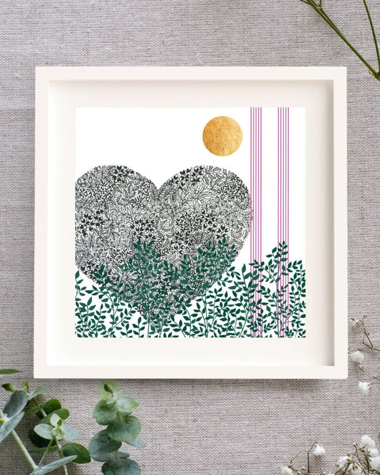 Image of a framed botanical art illustration. The frame is square, wooden, and white with a white mount. It is set on a linen cloth surrounded by baby's breath and eucalyptus.
The print is of a black pen illustration of a heart. Below the heart along the bottom of the image there are green leaves and branches. Up the right side of the print there are two strips of 5 pink lines, like music lines. At the top of the image there is a bright circle of hand-applied gold leaf.