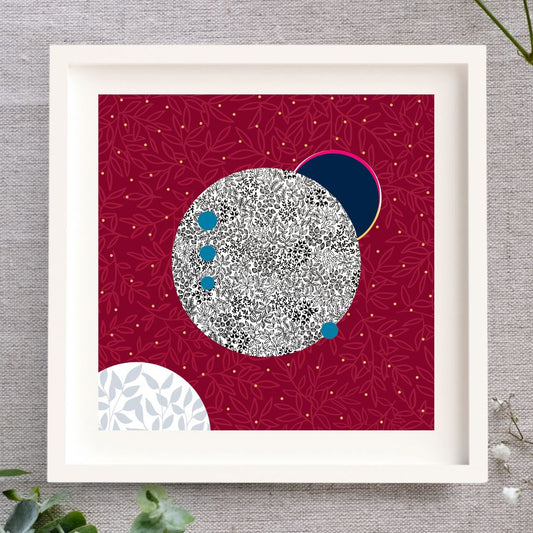 Irish Print, framed. Firey red background, gold leaf luminous stars. In the centre is a large moon illustrated with black pen leaves on a white moon surface. There are blue and white circles representing the moon and the Artemis spaceship. Set in a white frame.
