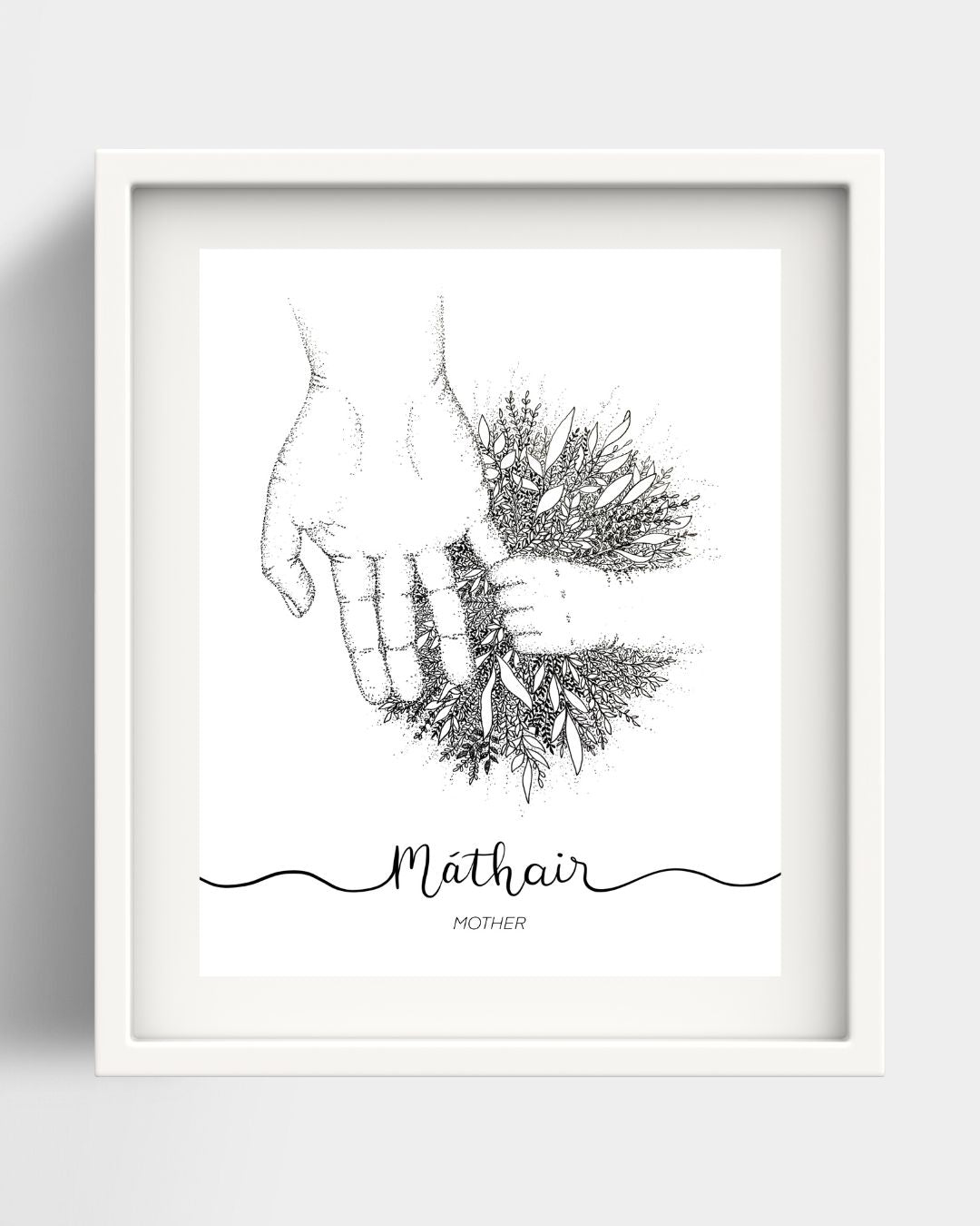 A framed art print of an adult hand holding a child's hand. Where the hands meet there is a big burst of foliage. Underneath the drawing the Irish word "Máthair" is handwritten in black script. Beneath that is the translation Mother. The background is white, the frame and the mount are also both white.