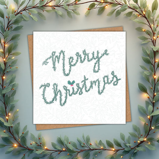 Irish Christmas card which says Merry Christmas, written in lettering made from leaves in a deep green. There's a little holly on the top of the i in Christmas. There is a faint leaf pattern in the background.