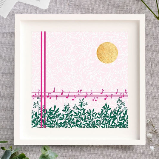 Midday Melody is a square design. The background is a soft light pink with a white leafy pattern. To the fore there are strong pink lines. Two vertical lines, and 5 horizontal lines forming a music stave with a scattering of pink notes on it. Along the bottom there are lots of green branches full of leaves. In the top right corner there is bright circle of gold leaf which has lovely texture to it. The design is framed in a white solid wood Irish made frame. It's displayed on a linen cloth.