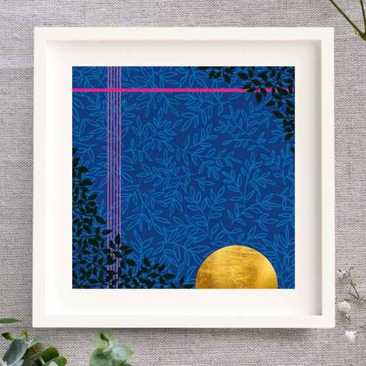 Midnight Magic is a framed art piece in a white mount and solid wood white frame. The illustration is moody and rich with a deep blue background, a subtle lighter blue leaf pattern layered on top, two striking pink lines, one at the top and one down the left side. There is a rich golden half sun/moon in gold leaf in the bottom right corner and there's some very dark green leaves in a triangle in the bottom left corner and top right corner. The frame is laid on a cloth with some foliage surrounding it.