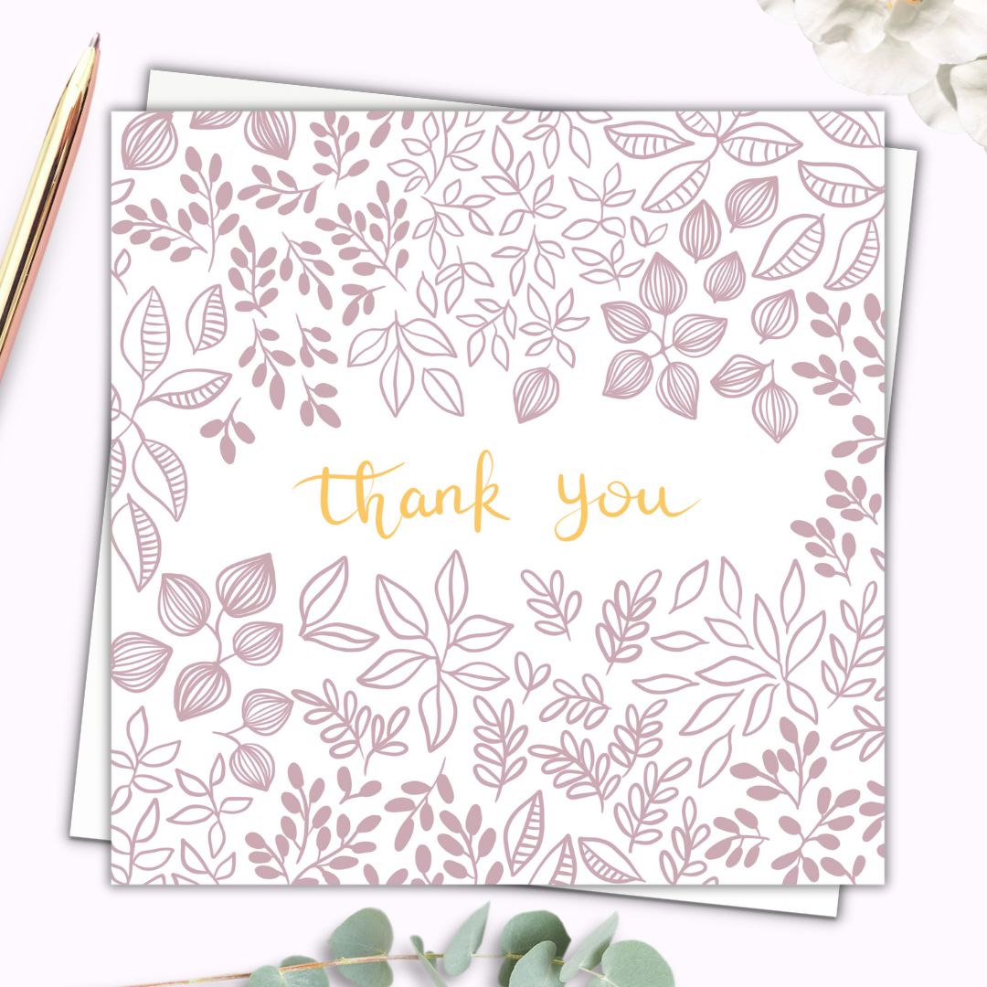 Pretty botanical Thank you card with dusty pink floral details and leaves and petals surrounding the words "Thank you" which is written in gold hand writing. The background of the botanical themed card is white so the details are clear and simple. The card is set on top of a plain white envelope.