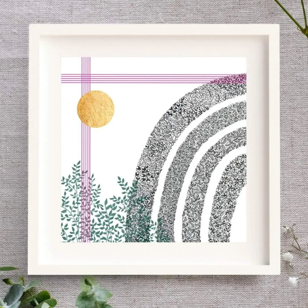 Image shows a framed art print lying on a linen cloth with sprinkles of baby's breath and eucalyptus around it. The frame is square and white. There is a white mount. The print is of a black and white pen illustration of a rainbow made of leaves. There's a cluster of green leaves in the bottom left corner. Straight up from there, there are five bright pink lines close together like music lines. The same 5 pink lines go across the top of the image, and lastly, there is a circle of hand-applied gold leaf.