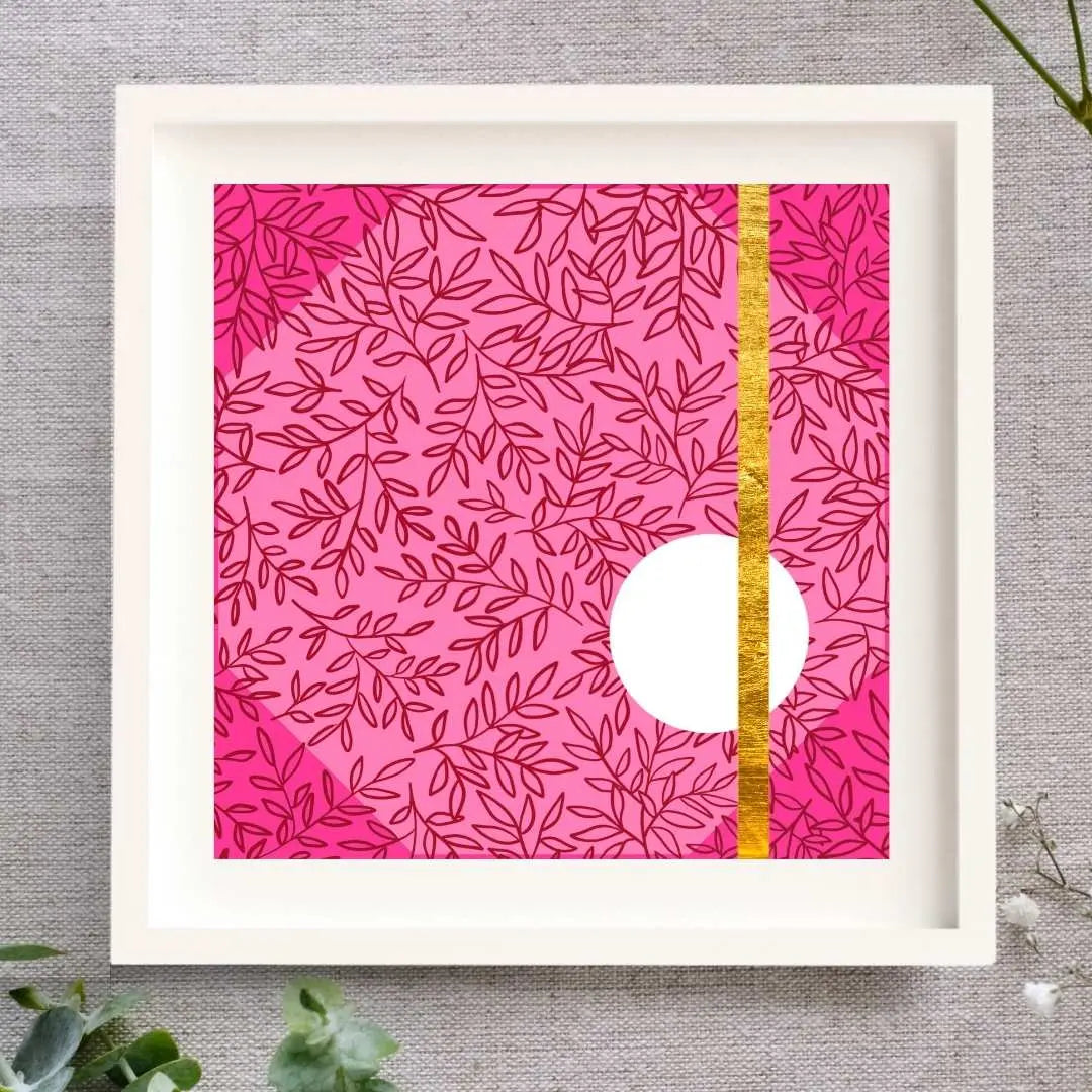 Framed Irish artwork with a light pink background. Layered on that is a dark pink leaf pattern and a deeper pink triangle in each corner. In the lower right side of the design, there's a medium clean white circle. There's a gold line made from gold leaf that goes from the top of the design to the bottom of the design going through the circle. The print is in a white mount and a solid wood white frame. It's square. It's on a natural cloth background and there are some leaves and buds around it.