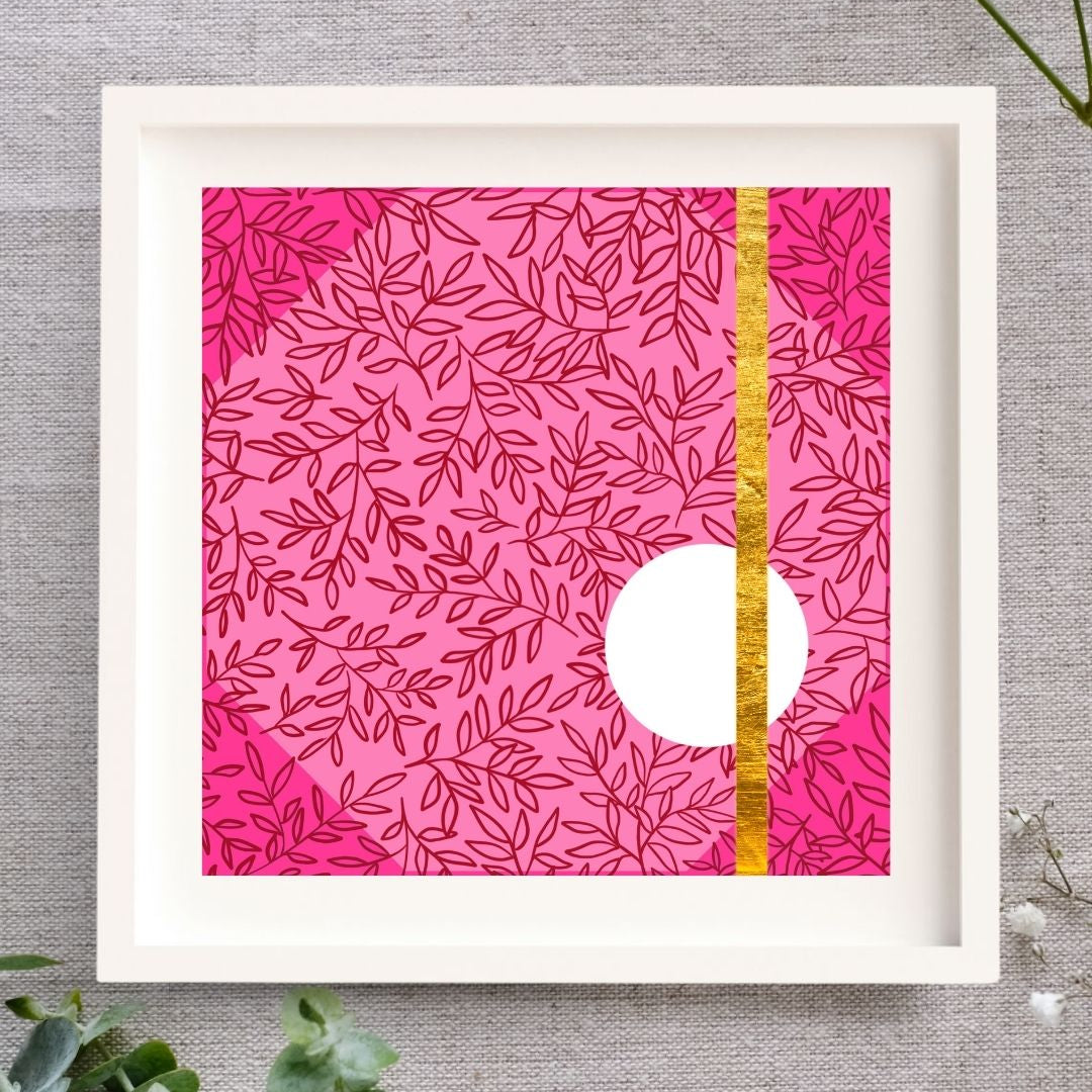 Framed Irish artwork with a light pink background. Layered on that is a dark pink leaf pattern and a deeper pink triangle in each corner. In the lower right side of the design, there's a medium clean white circle. There's a gold line made from gold leaf that goes from the top of the design to the bottom of the design going through the circle. The print is in a white mount and a solid wood white frame. It's square. It's on a natural cloth background and there are some leaves and buds around it.