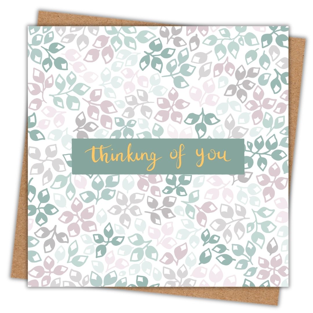 Botanical themed greeting card with simple floral buds of different colours. The colour palette is various shades of green, grey and dusty pink. In the centre of the card are the words "thinking of you" in gold writing on a dark green background. The card is lying on a kraft brown envelope.