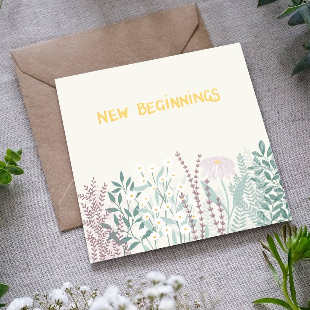 Greeting card with 'New Beginnings' text and floral design on a gray surface with an envelope.