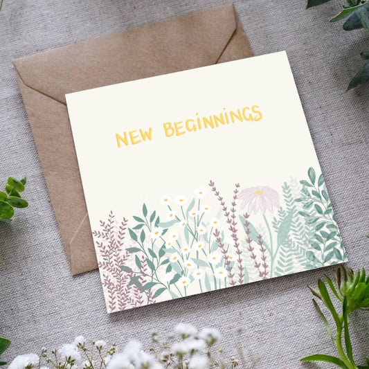 Greeting card with 'New Beginnings' text and floral design on a gray surface with an envelope.