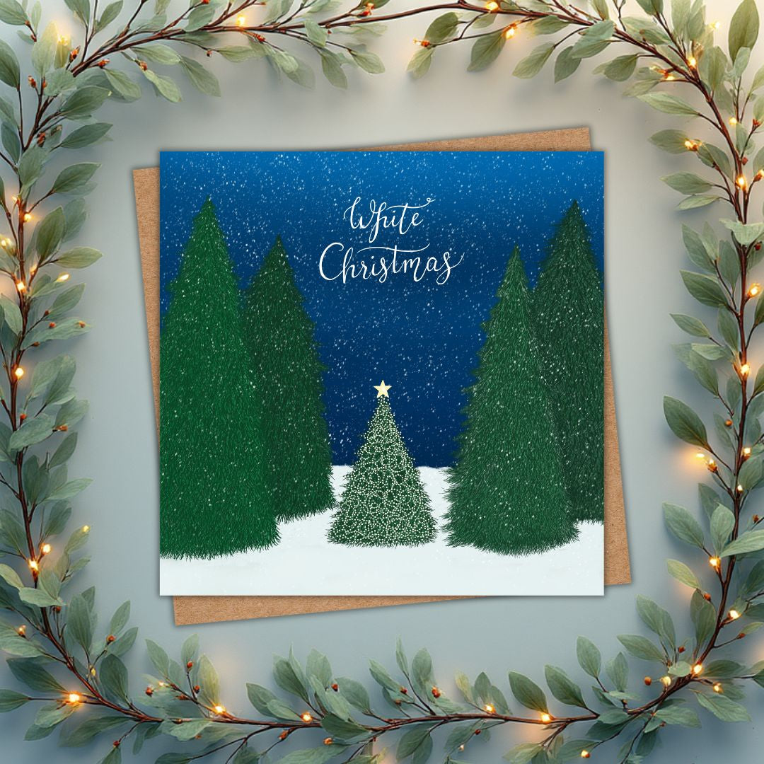 Christmas card with large green trees surrounding one small little tree that's lit up and has a gold star on top. The scene is set in a forest with a deep blue sky and snow falling. Above, 'White Christmas' is written in Calligraphy hand writing.