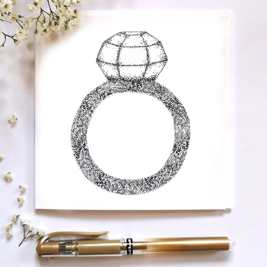 Image shows drawing of a Diamond ring drawn from flowers and black and white dots. the diamond is made entirely from different sized dots. image is laid on a cream surface with arrangements surrounding it to show the image dressed up. 