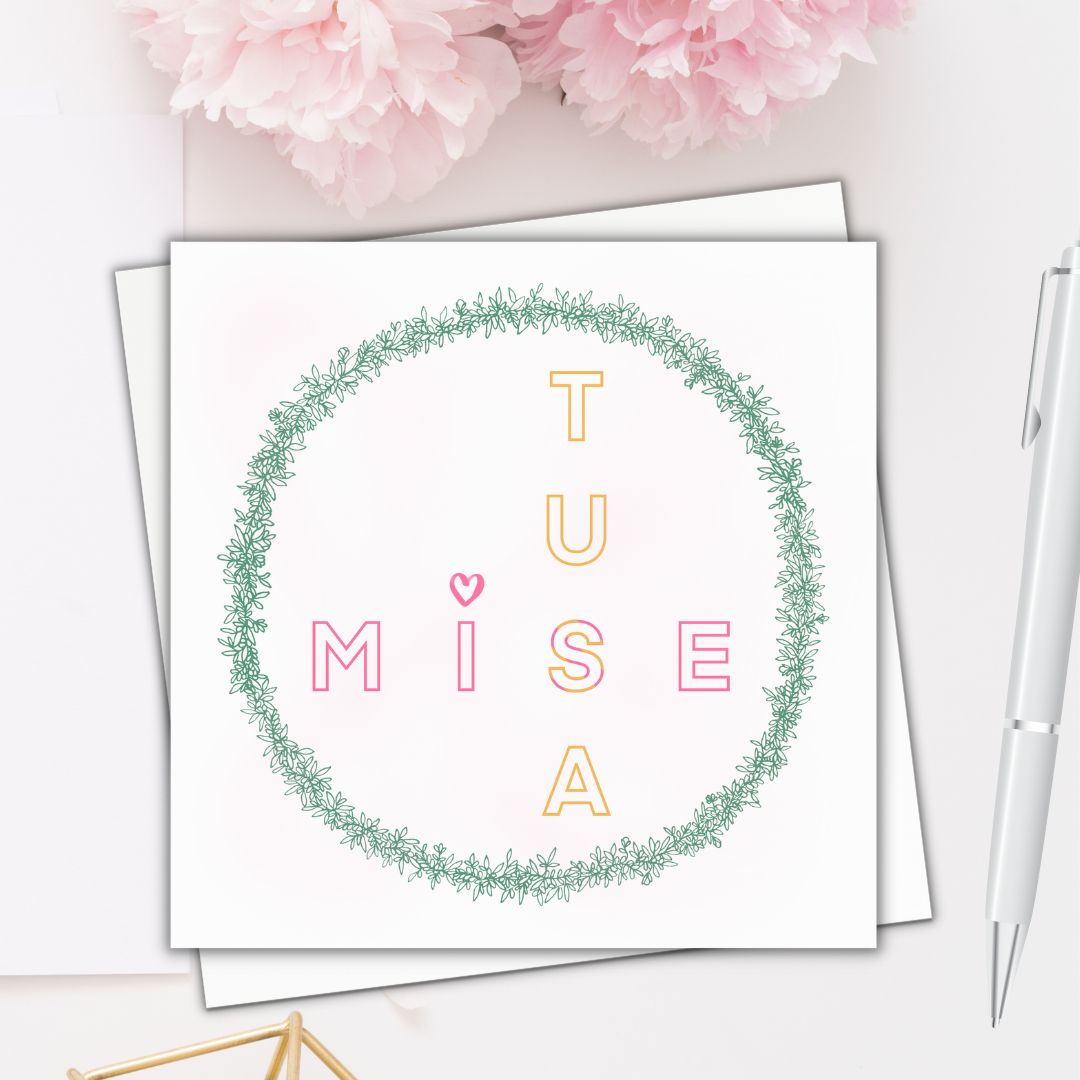 Image shows card illustration with the saying Irish Mise Tusa meaning Me You. Mise is drawn  going across the card whilst Tusa is drawn going down the card. Mise is drawn in pink block capitals and Tusa is drawn in yellow block capitals. The I in Mise has a heart drawn on top. the text is circled by green petal flower and plant drawings. Image is laid on a cream surface with pink flowers at the top to dress up the image.