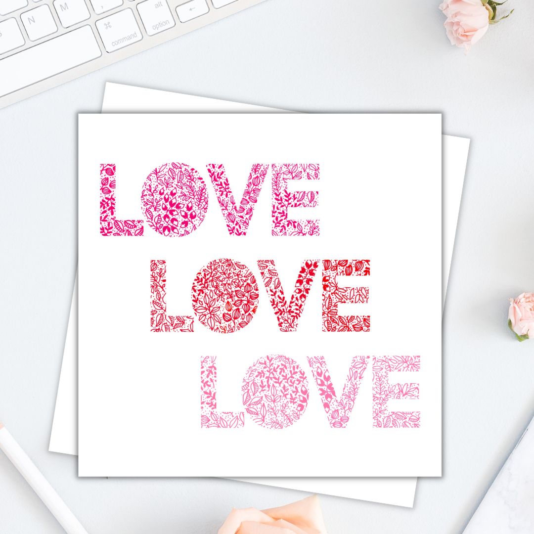 Image shows LOVE LOVE LOVE illustration card. Illustration is made from a variety of floral drawings red orange and pink. image is laid on a cream surface. 